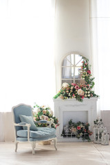 Bright room, fireplace and blue armchair. A lot of flowers and candles.