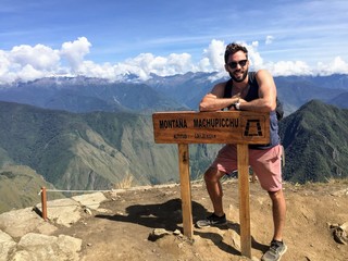 A young male tourist standing beside the sign for the summit of Machu Picchu mountain at the famous...