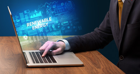 Fototapeta premium Businessman working on laptop with RENEWABLE ENERGY inscription, cyber technology concept