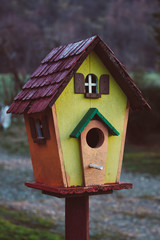 A small colorful wooden bird house outside in the garden, vertical image.