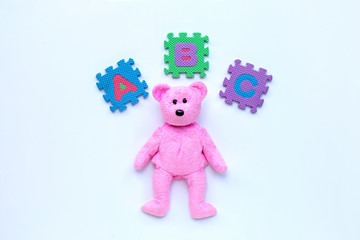 Pink beartoy with english alphabet puzzle on white background. Education concept.