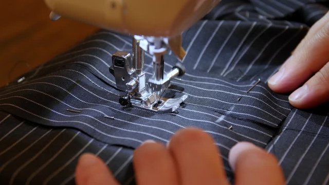 Seamstress sews clothes made of black striped cloth on a sewing machine. Work by the light of the built-in hardware lamp. Steel needle with looper and presser foot close-up.