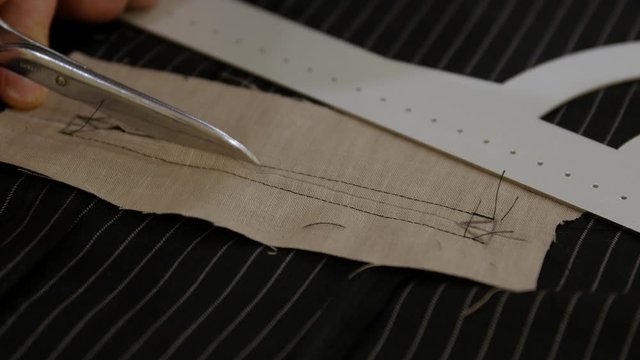 Fashion designer hands opening the Besom pockets by cutting the fabric. found on a tuxedo jacket or trousers A pocket is a bag receptacle either fastened to or inserted in an article of clothing 