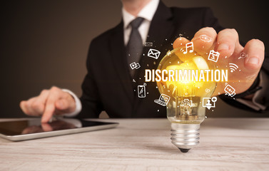Businessman holding light bulb with DISCRIMINATION inscription, social media concept