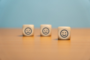 Happy Smiley on wooden dice in front of unhappy blurred smileys