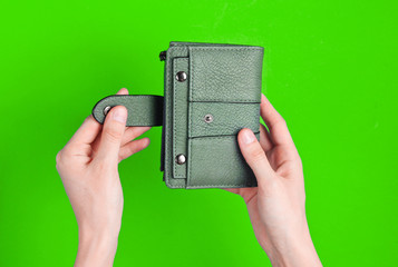 Women's hands open leather wallet on green background. Top view