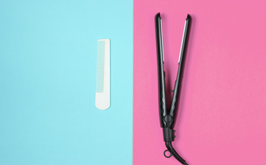 Minimalistic beauty and fashion still life. Comb and hair straightener on blue pink background. Top view, flat lay