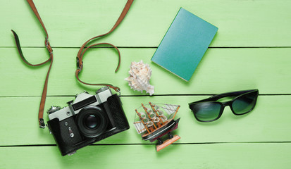 Traveler accessories, retro camera on green wooden background. Trip on the beach, vacation. Summer minimalistic background. Flat lay tourism allegory..Top view.