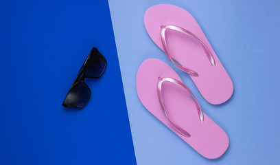 Summer still life. Beach accessories. Fashionable beach pink flip flops, sunglasses on blue  paper background. Flat lay. Top view