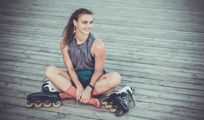 Young happy woman roller skater sitting on  wooden boards outdoors. Sport lifestyle