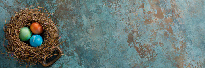 Easter eggs in a bird's nest on a textural background. Easter celebration concept. Copy space. Flat lay. Banner.