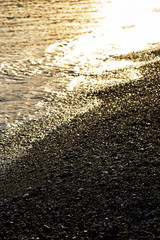 Golden pebbles and seawater in the sunset lights. Seashore and coastline. Nature background