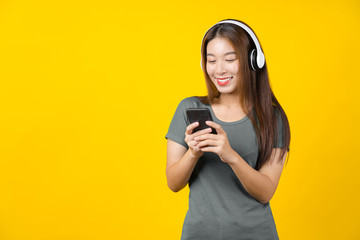 Happiness Asian smiling young woman wearing technology wireless headphones for listening the music via smart mobile phone on isolated yellow color background, Lifestyle and leisure with hobby concept