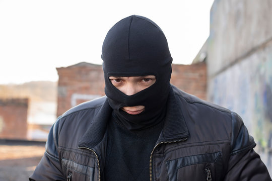 a bandit, a terrorist in a black mask and jacket in a slum and on the territory of an abandoned destroyed building in a deprived area