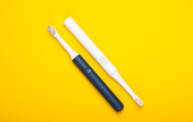 Two Modern electric toothbrushes on yellow background. Top view. Teeth care. Minimalism