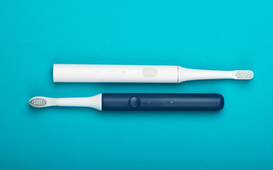 Two Modern electric toothbrushes on blue background. Top view. Teeth care. Minimalism