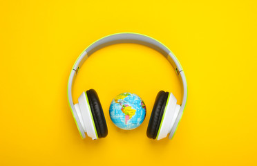 World song. Global music chart. The music of earth. Stereo headphones and a globe on yellow background. Top view