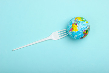 Eco still life. Save the planet concept. Plastic free. Globe impaled on a plastic fork on a blue background. Minimalism