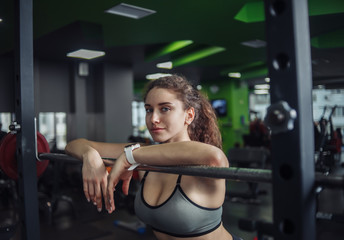 Fototapeta na wymiar Tired fit woman in sportswear leaning on barbell in the gym