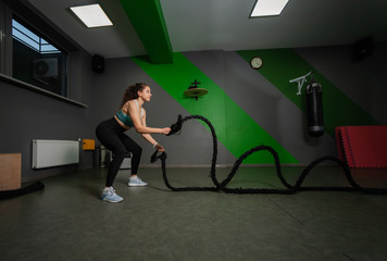 Fototapeta premium Young fit woman doing exercise with battle ropes in training class. Functional training, workout process.
