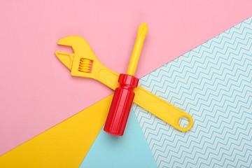 Toy wrench and screwdriver on a colored pastel background. Top view. Minimalism