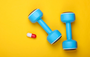 Pharmacology in sports. Dumbbell and capsule on a yellow background. Vitamins, steroids. Top view
