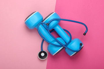 The concept of a healthy lifestyle and health care. Dumbbell with a stethoscope on a pink pastel background. Top view