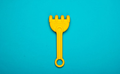 Children's rake for a sandbox or a beach on blue studio background. Top view