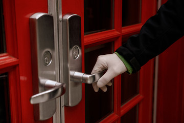 Man's hand wearing a white plastic latex glove opens the red door. Protection, safety, corona virus issues concept. Close up