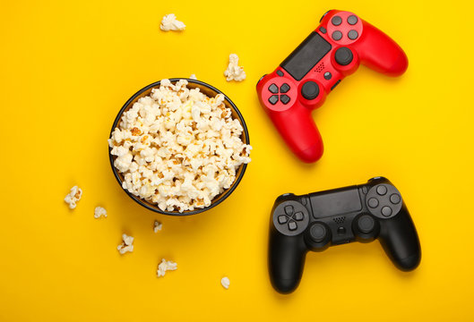 Two gamepads and a bowl of popcorn on yellow background. Gaming, leisure and entertainment concept. Top view