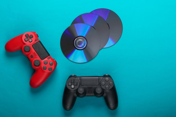 Two gamepads and cd compact discs on blue background. Gaming, entertainment concept. Top view