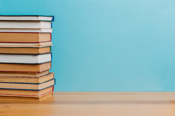 A simple composition of many hardback books, raw books on a wooden table and a bright blue background. Going back to school. Copy space. Education.