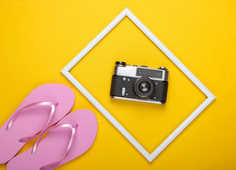 Flip flops and retro camera on yellow background with white frame. Studio shot. Creative beach resort flat lay, travel. Top view. Minimalism