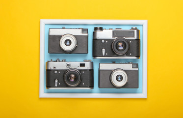 Obraz premium Many Retro cameras on yellow background with photo frame. Studio shot. Creative flat lay. Top view. Minimalism