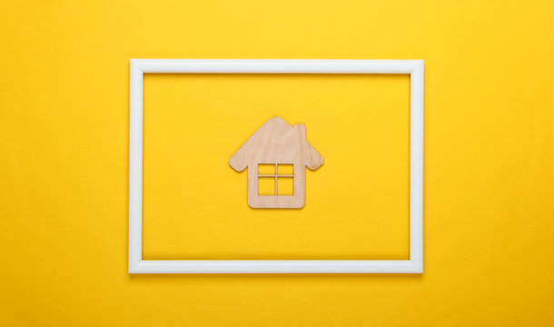 Mini wooden house on yellow background with white frame. Studio shot. Creative flat lay. Top view. Minimalism
