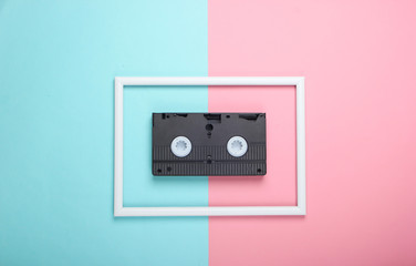 Video cassette on pink blue pastel background with white frame. Studio shot. Creative retro flat lay. Top view. Minimalism. 80s