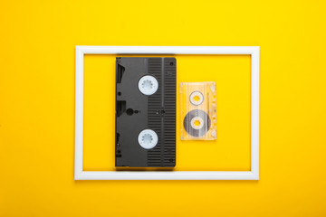 Video and audio cassette on yellow background with white frame. Studio shot. Creative retro flat lay. Top view. Minimalism. 80s