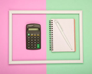 Calculator and notebook in white frame on pink green pastel background. Top view