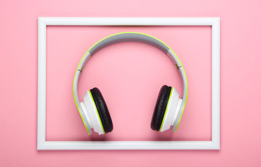 Stylish wireless stereo headphones on pink pastel background with white frame. Music lover. Gadgets. Top view.