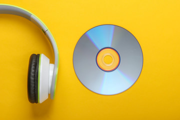 Half of stylish stereo headphones with cd disc on yellow background. Music lover. Retro 90s. Top...