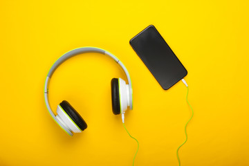 Wired stereo headphones with smartphone on yellow background. Millennial stuff. Music lover. Top view. Minimalism