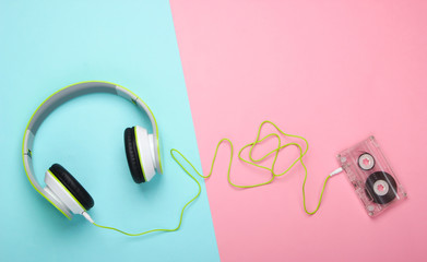 Stylish wired stereo headphones with audio cassette on pink blue pastel background. Music lover. Retro 80s. Top view.