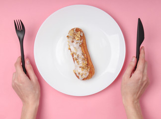 eclair on plate. Pink pastel background. Dessert. Top view, minimalism