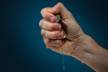 Various coins from around the world held in clenched hand. Male hand squeezes coins. Conceptual...