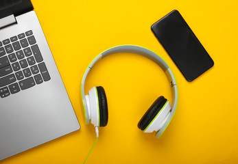 Laptop with stereo headphones and smartphone on yellow background. Flat lay composition. Modern gadgets. Top view