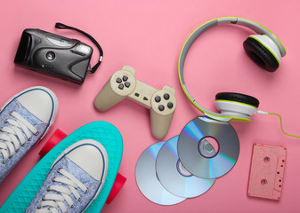 Flat lay hipster composition. Cruiser board, stereo headphones, audio cassette, cd discs, retro camera on pink background. Retro 80s entertainments. Top view
