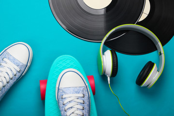 Flat lay hipster stuff. Sneakers on cruiser board, stereo headphones, vinyl record on a blue background. Retro 80s entertainments. Top view