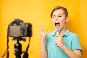 Portrait of young teen boy singing over the microphone isolated on yellow background