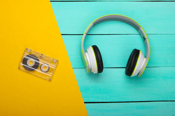 Stereo headphones with audio cassette on blue wooden table. Music lover. Retro 80s. Top view.