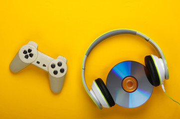 Stereo headphones with gamepad, cd disc on yellow background. Gaming, leisure and entertainment concept. Top view.